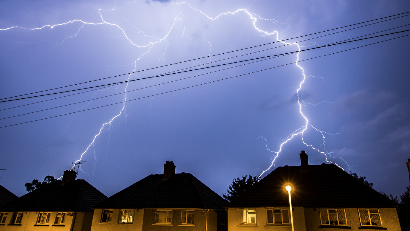 A fork of lightning illuminating the sky above a row of houses.