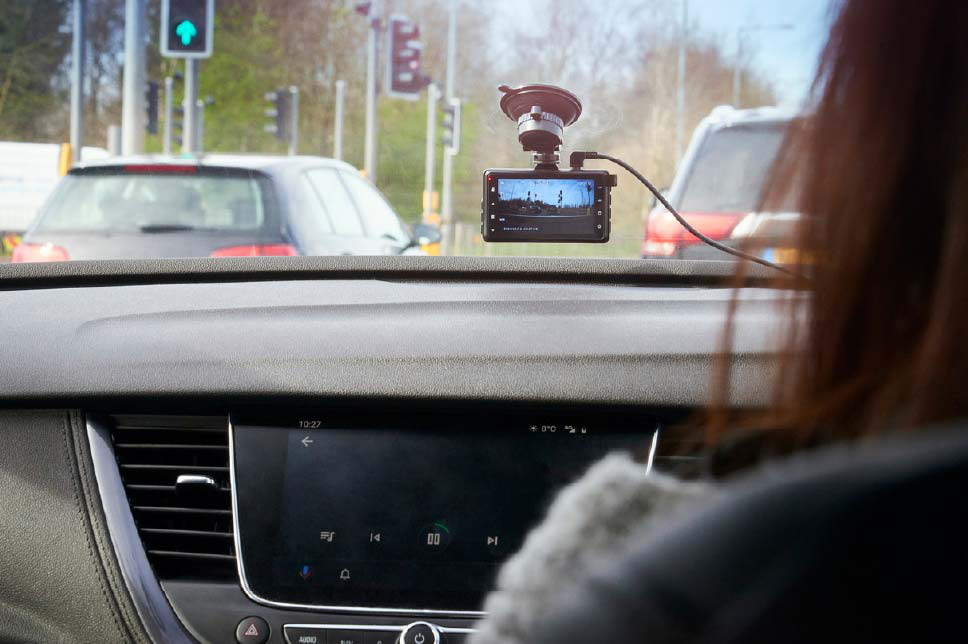 Over the shoulder shot of a woman driving her car with a dash cam attached to the windscreen recording footage of the road ahead.