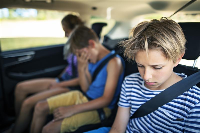Three children sitting in the back of a car, one of whom has their head in their hands.